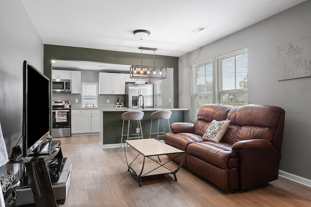 living room featuring baseboards, light wood finished floors, and visible vents