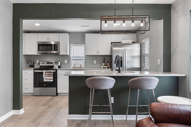 kitchen featuring light stone counters, light wood-style floors, a breakfast bar, stainless steel appliances, and white cabinets