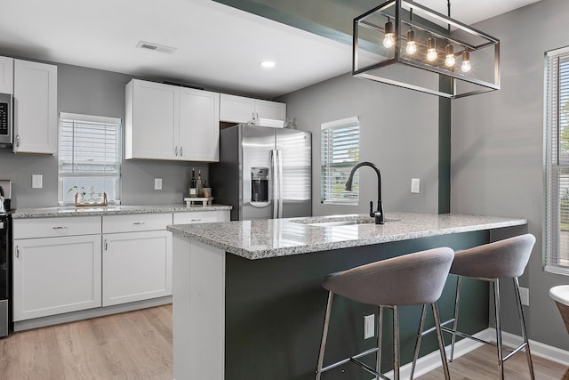 kitchen with a sink, a breakfast bar, light wood-type flooring, stainless steel appliances, and visible vents