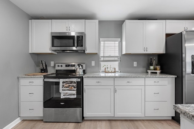 kitchen featuring white cabinets, light stone countertops, stainless steel appliances, and light wood finished floors