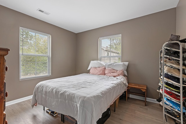 bedroom with light wood-type flooring, baseboards, visible vents, and multiple windows