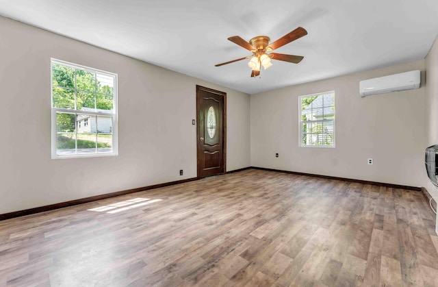 unfurnished living room with an AC wall unit, a ceiling fan, baseboards, and wood finished floors
