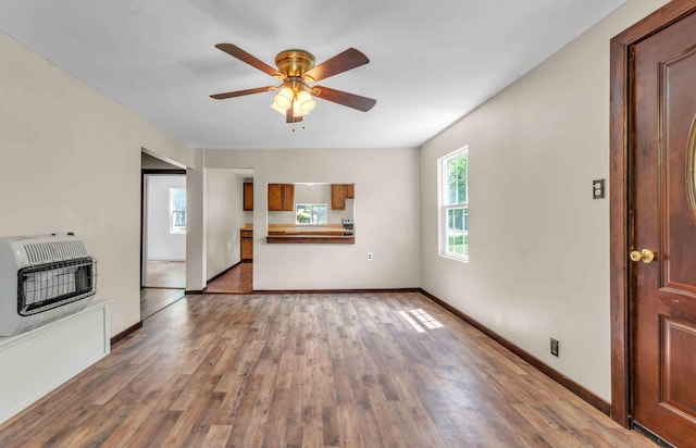 unfurnished living room with baseboards, heating unit, ceiling fan, and wood finished floors