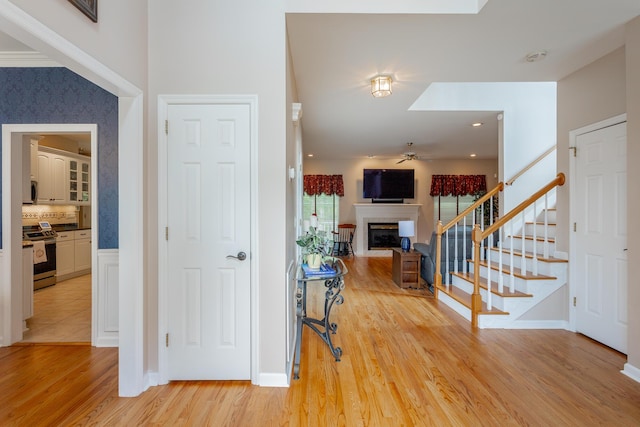 entrance foyer with a fireplace, light wood-style floors, stairs, a ceiling fan, and baseboards