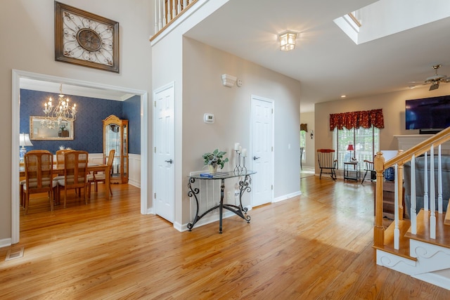 entrance foyer featuring a skylight, a wainscoted wall, light wood finished floors, a notable chandelier, and stairs