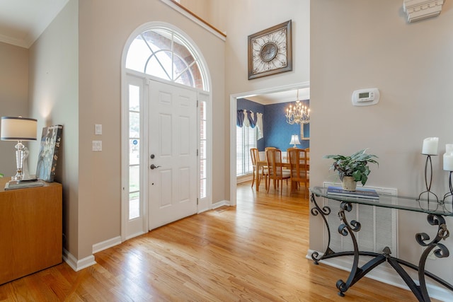 foyer entrance with baseboards, a notable chandelier, ornamental molding, and light wood-type flooring