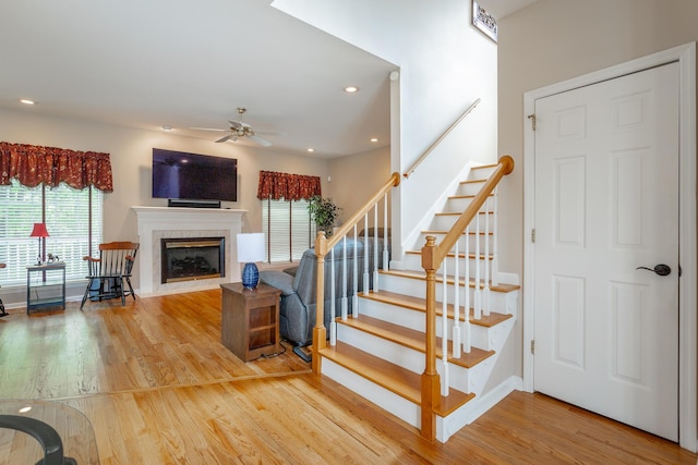 stairway featuring a premium fireplace, a ceiling fan, a healthy amount of sunlight, and wood finished floors