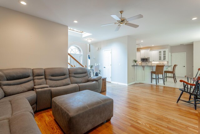 living area featuring a ceiling fan, stairs, baseboards, light wood finished floors, and recessed lighting