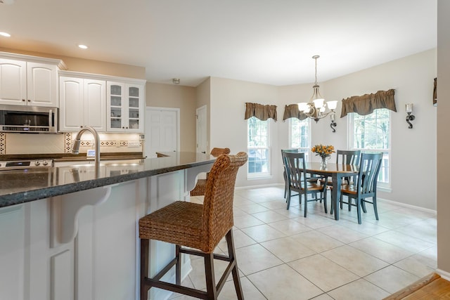 kitchen with a breakfast bar area, backsplash, baseboards, stainless steel microwave, and a notable chandelier