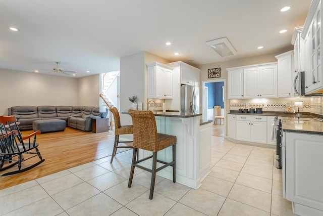 kitchen with white cabinets, light tile patterned flooring, appliances with stainless steel finishes, a kitchen breakfast bar, and open floor plan