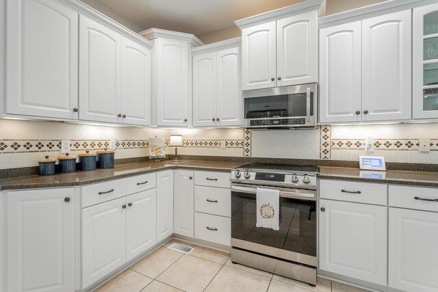 kitchen featuring backsplash, light tile patterned floors, glass insert cabinets, stainless steel appliances, and white cabinetry