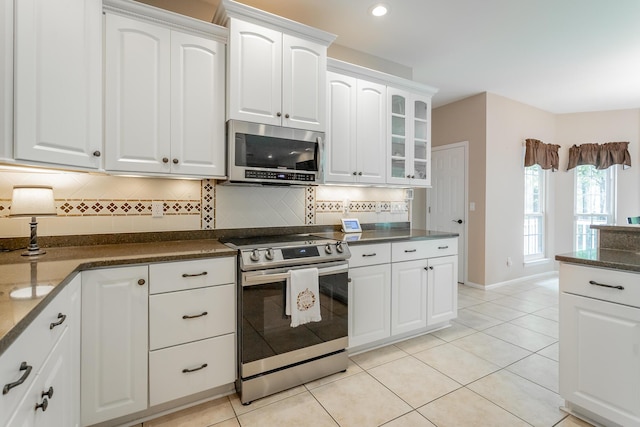 kitchen with glass insert cabinets, appliances with stainless steel finishes, tasteful backsplash, and light tile patterned floors