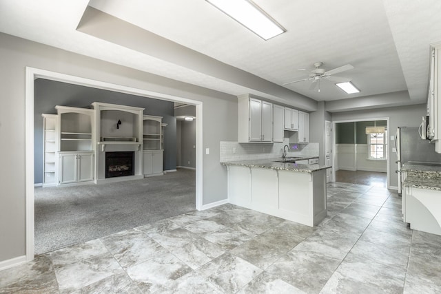 kitchen with baseboards, light stone countertops, a ceiling fan, and a peninsula