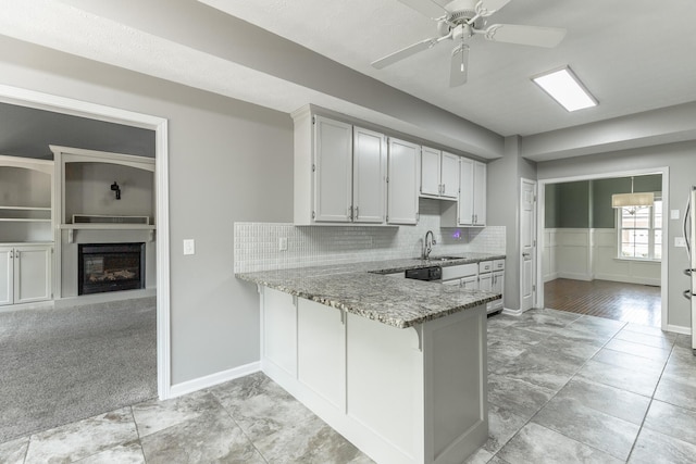 kitchen featuring light stone counters, tasteful backsplash, a glass covered fireplace, a peninsula, and a ceiling fan