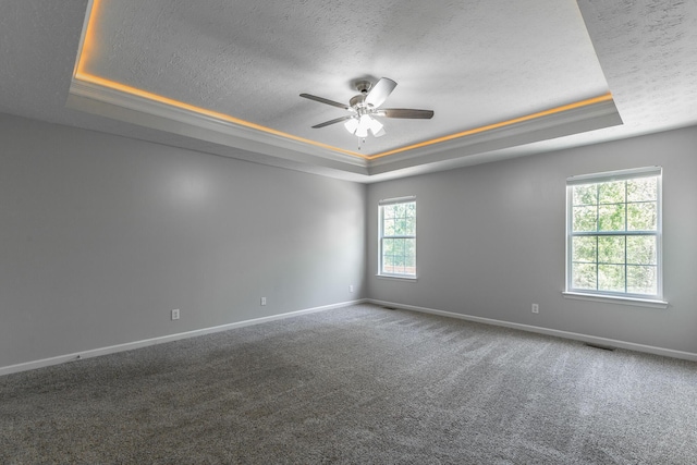 carpeted spare room with a textured ceiling, a ceiling fan, a raised ceiling, and baseboards