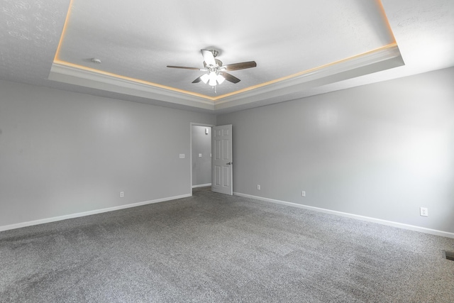 carpeted spare room featuring a ceiling fan, a tray ceiling, and baseboards