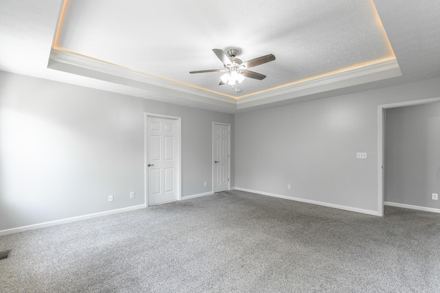 carpeted spare room with a raised ceiling, a ceiling fan, visible vents, and baseboards