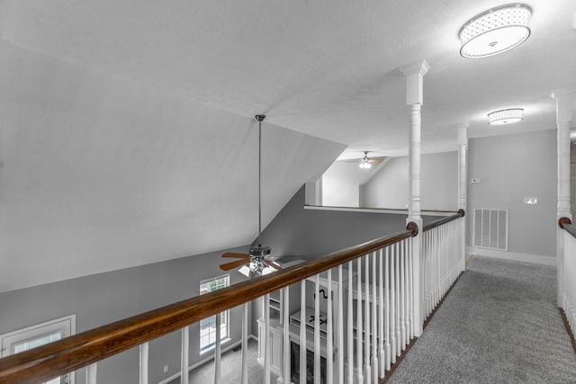 hallway featuring decorative columns, visible vents, carpet, a textured ceiling, and lofted ceiling
