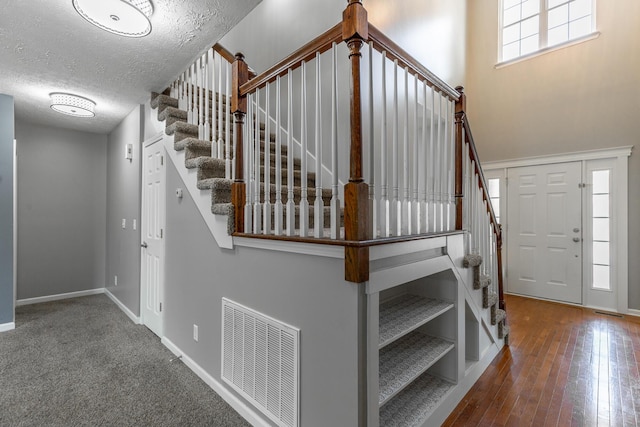 stairs featuring a textured ceiling, visible vents, wood finished floors, and baseboards