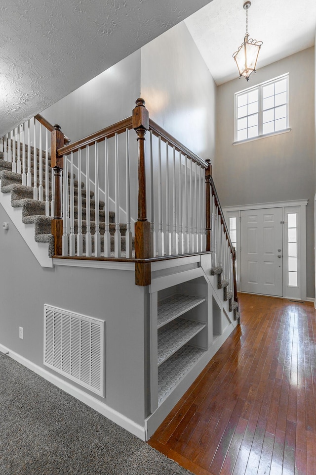staircase with a textured ceiling, visible vents, a chandelier, baseboards, and wood-type flooring