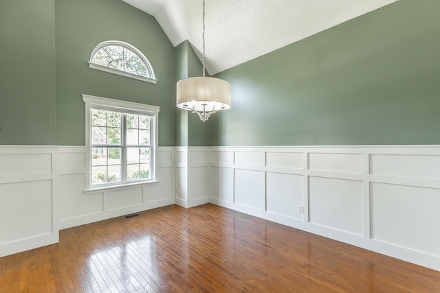 unfurnished dining area featuring a chandelier, visible vents, a decorative wall, wainscoting, and lofted ceiling