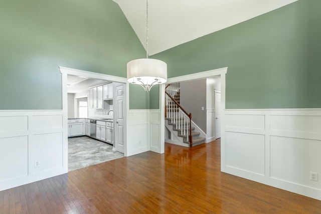 unfurnished dining area with a sink, a wainscoted wall, wood-type flooring, a decorative wall, and stairs