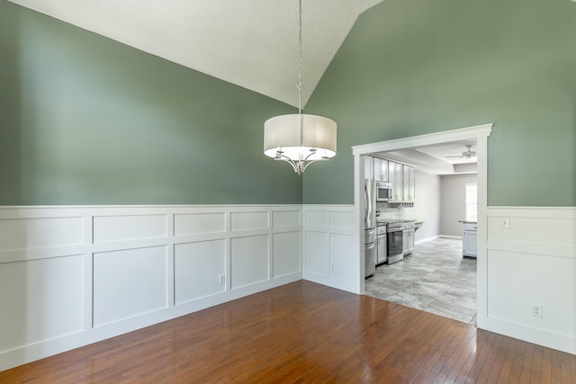 unfurnished dining area with a wainscoted wall, a decorative wall, hardwood / wood-style flooring, and high vaulted ceiling