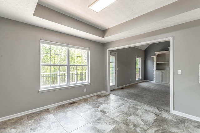 spare room with a tray ceiling, visible vents, a wealth of natural light, and baseboards