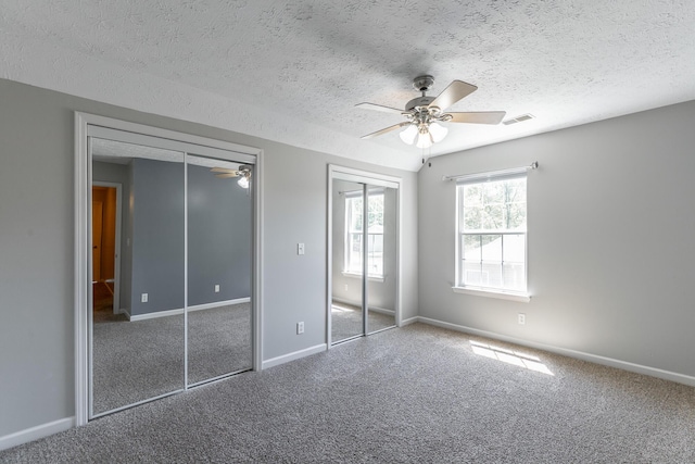 unfurnished bedroom featuring multiple closets, carpet flooring, baseboards, visible vents, and a textured ceiling