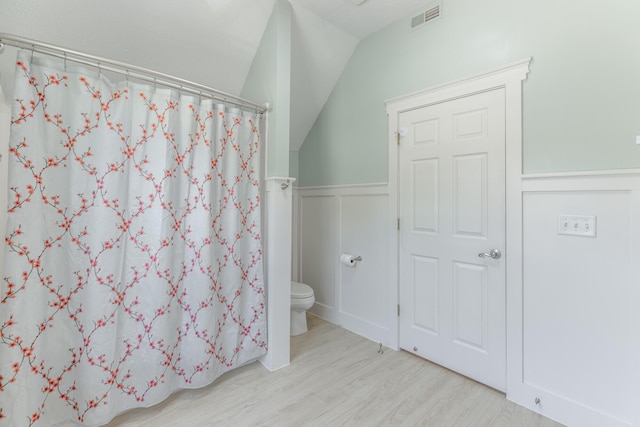 full bathroom featuring wood finished floors, wainscoting, toilet, visible vents, and lofted ceiling
