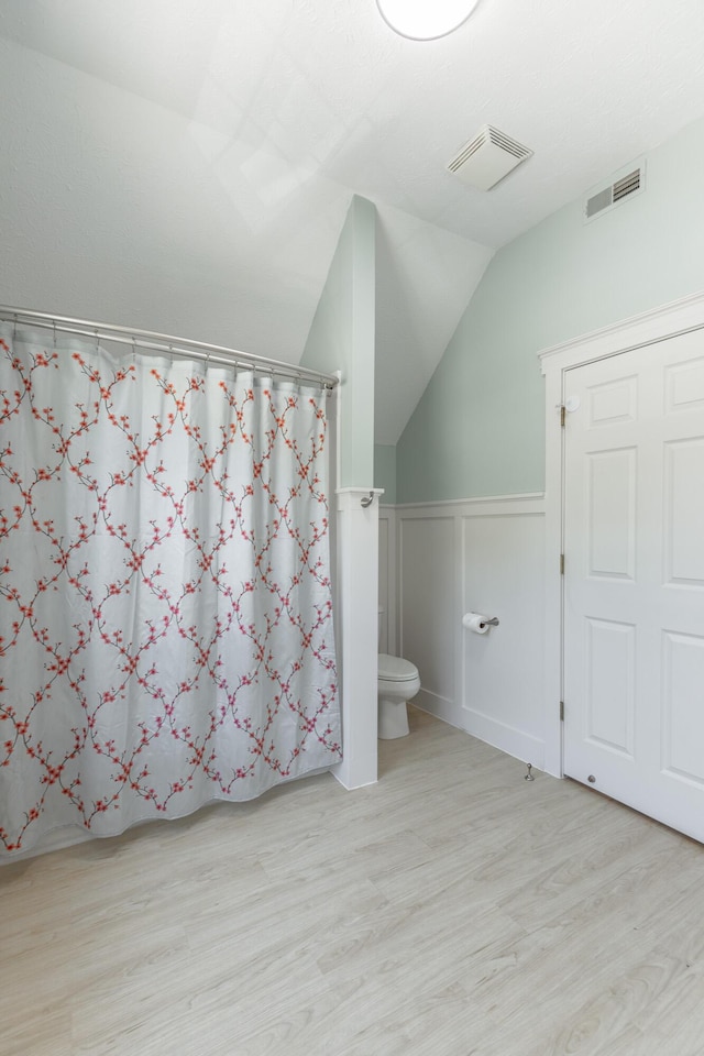 bathroom with lofted ceiling, wood finished floors, visible vents, and toilet