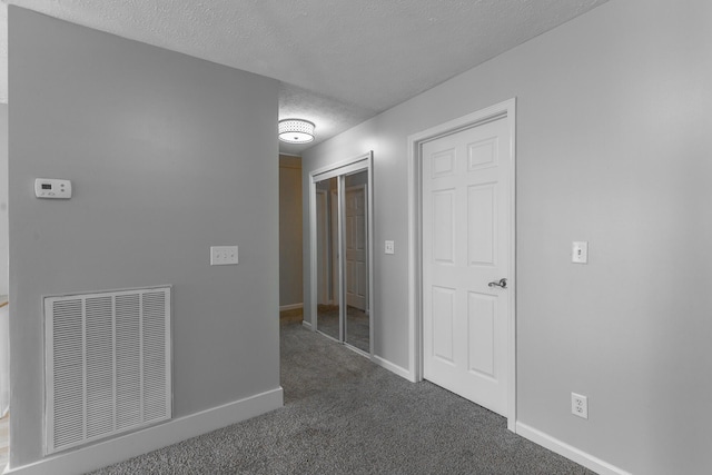 interior space featuring a textured ceiling, carpet flooring, visible vents, baseboards, and a closet
