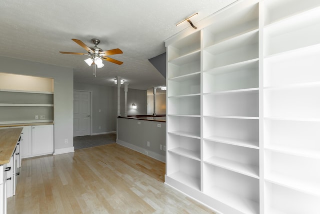 interior space featuring light wood finished floors, a ceiling fan, a textured ceiling, and baseboards