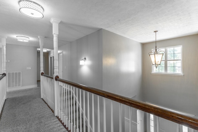 hallway with a textured ceiling, visible vents, baseboards, carpet floors, and a notable chandelier