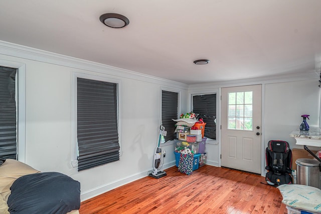 doorway featuring ornamental molding, light wood-style flooring, and baseboards