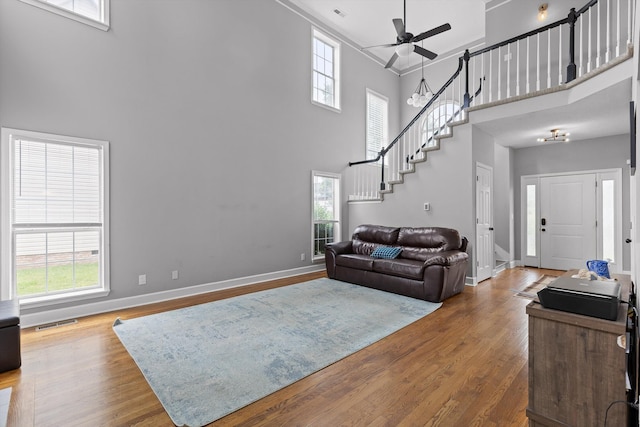 living area with a ceiling fan, baseboards, a towering ceiling, visible vents, and stairway
