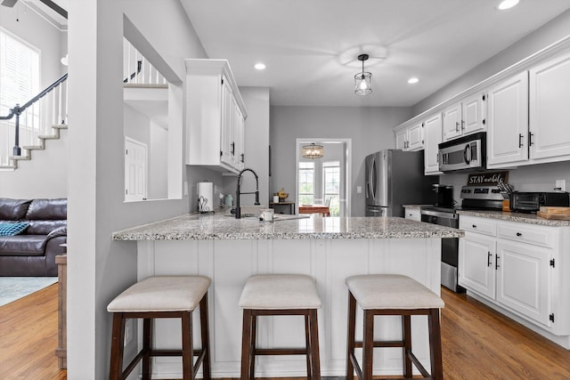 kitchen with a peninsula, white cabinetry, a sink, light wood-style flooring, and appliances with stainless steel finishes