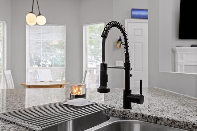 interior details featuring light stone counters, a sink, and pendant lighting
