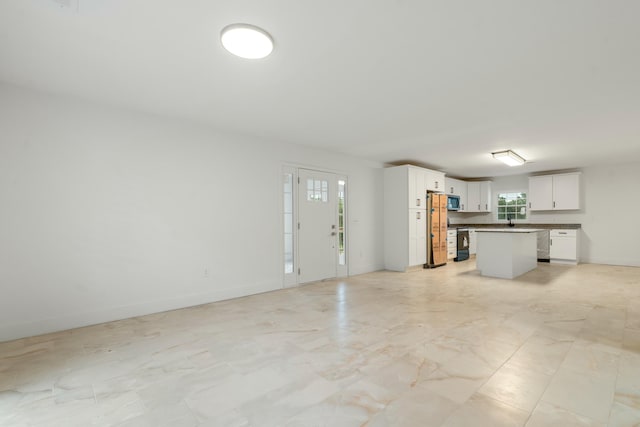 unfurnished living room with a sink, a wealth of natural light, and baseboards