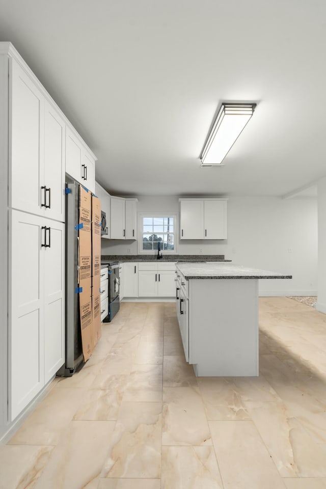 kitchen featuring fridge, stainless steel microwave, black / electric stove, a kitchen island, and white cabinets