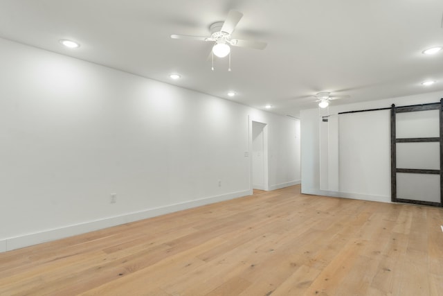 interior space featuring light wood-style floors, a ceiling fan, baseboards, and a barn door