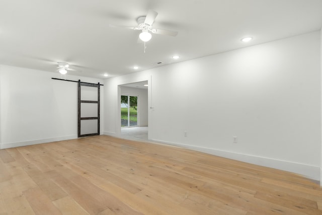 unfurnished room with baseboards, a barn door, ceiling fan, and light wood finished floors