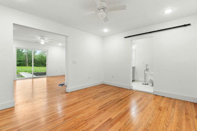 unfurnished room featuring baseboards, a barn door, a ceiling fan, and light wood finished floors