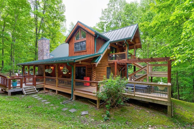 back of house with metal roof, a chimney, a deck, log siding, and a yard