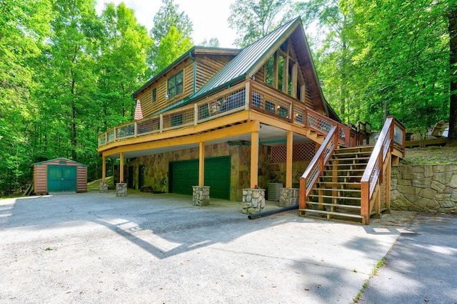 view of front of home with a garage, stone siding, a storage unit, metal roof, and driveway