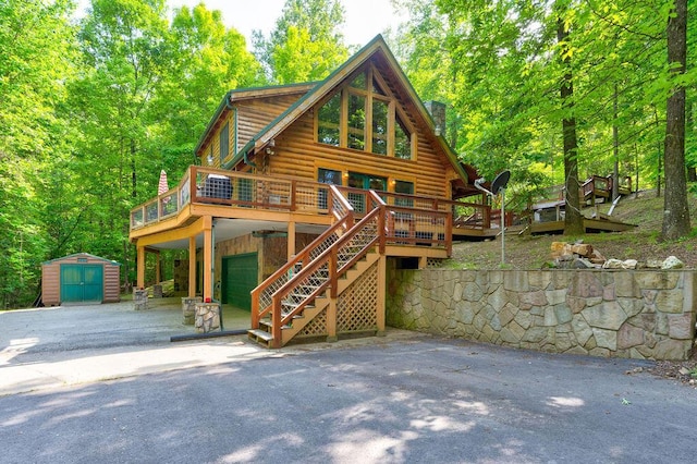 view of front of house with a garage, a deck, a shed, log siding, and an outbuilding