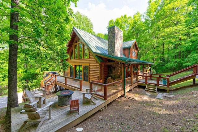 exterior space featuring log exterior, a wooden deck, a chimney, and an outdoor fire pit
