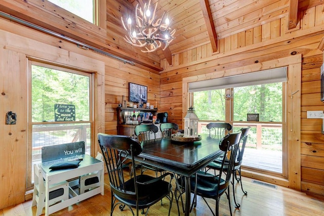 dining space featuring wood walls, an inviting chandelier, visible vents, and light wood-style floors
