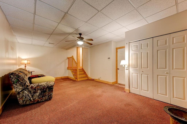 living area with a ceiling fan, baseboards, a drop ceiling, and carpet