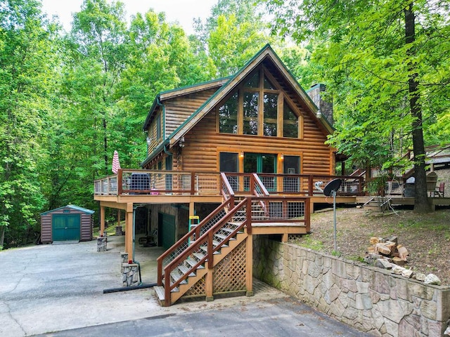 view of front of house with an outdoor structure, a wooden deck, a shed, and log exterior